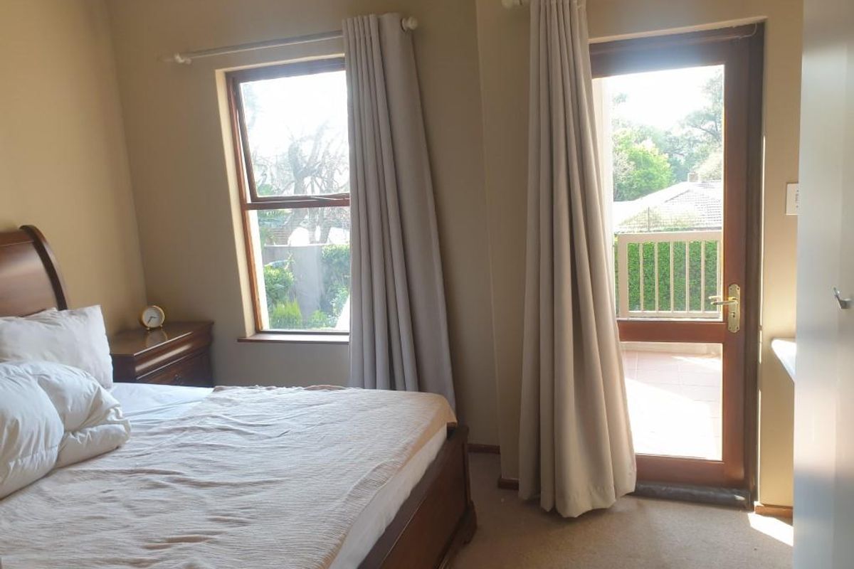 A bedroom featuring carpeted flooring, a timber-framed window, and a door providing direct access to an outdoor balcony area.