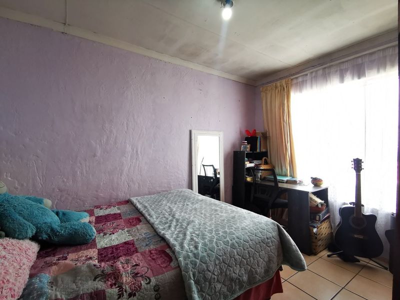 A bedroom featuring tiled flooring and a ceiling light fixture, with visible signs of wear on the walls and ceiling.