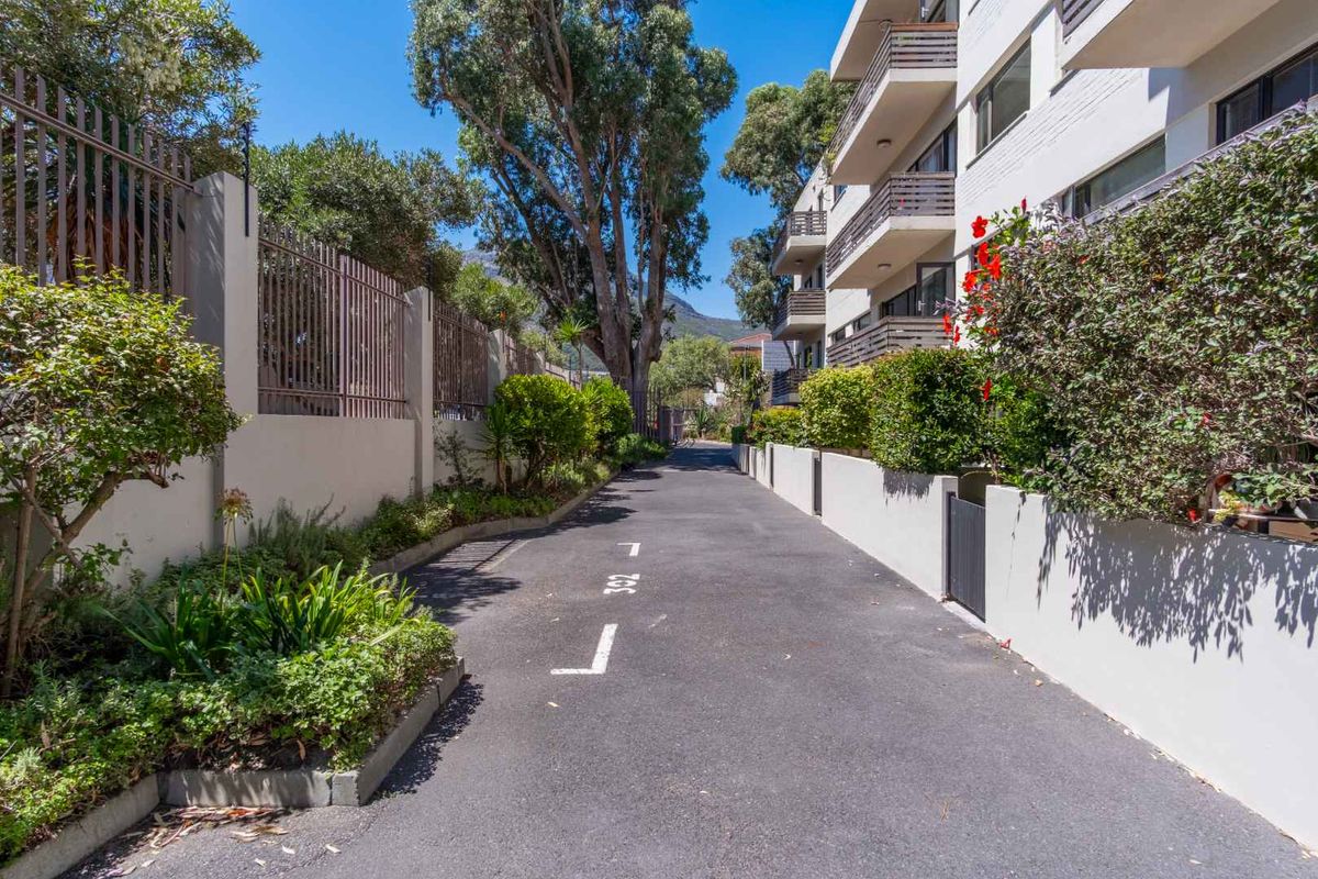 A well-maintained paved driveway and access path leading alongside the apartment building, featuring landscaped garden borders and secure boundary fencing.