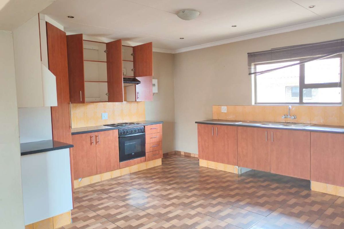 A functional kitchen featuring laminate cabinetry, built-in oven with hob, extractor fan, and double sink with tiled backsplash and flooring.