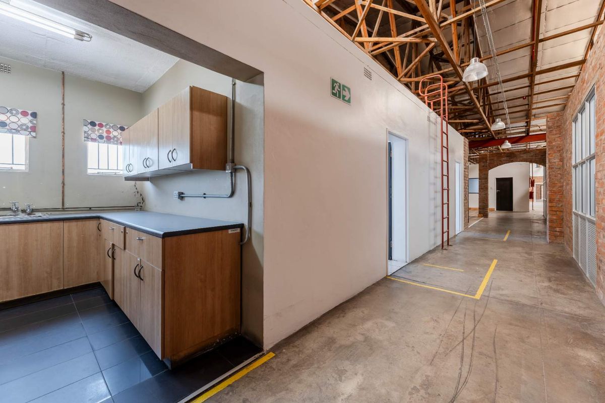 Industrial interior space featuring a kitchenette with built-in cabinetry, exposed timber roof trusses, and a spacious corridor with concrete flooring.