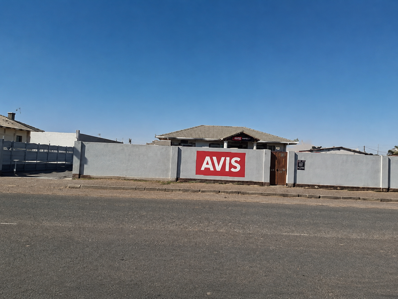 Street view of a commercial property featuring a prominent perimeter wall, gated entrance, and tiled roof structure.