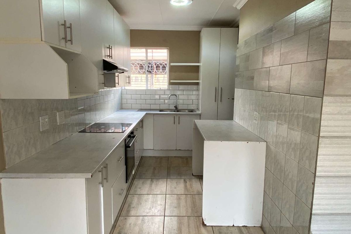 A functional galley-style kitchen featuring white cabinetry, built-in oven and hob, tiled backsplash, and neutral floor tiles.