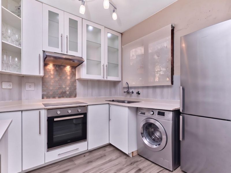 Modern kitchen featuring white cabinetry, hexagonal tile splashback, stone countertops, integrated oven and hob, and space for laundry appliances.