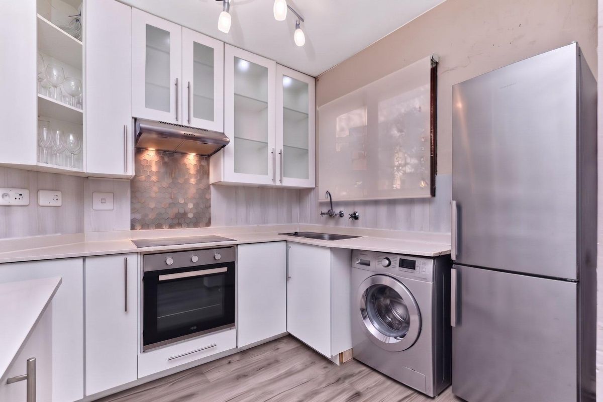 Modern kitchen featuring white cabinetry, hexagonal tile splashback, stone countertops, integrated oven and hob, and space for laundry appliances.