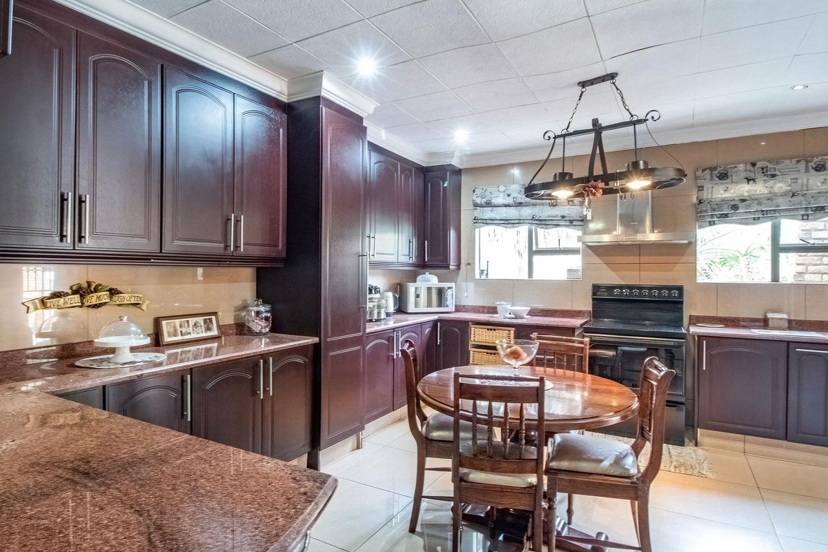 A spacious kitchen featuring dark wood cabinetry, granite countertops, a built-in extractor fan, and tiled flooring with an integrated dining area.