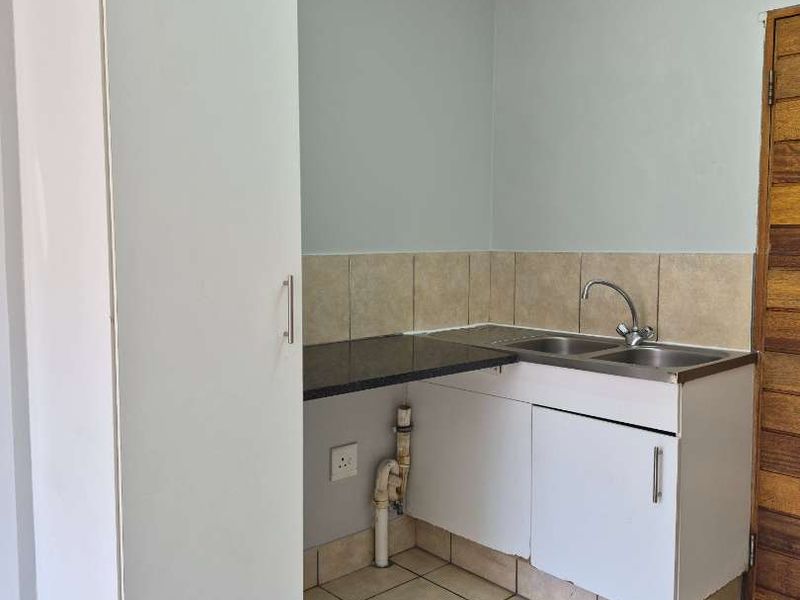 A compact kitchen area featuring built-in cabinetry, a stainless steel sink, tiled backsplash, and tiled flooring, currently in need of minor cosmetic updates.