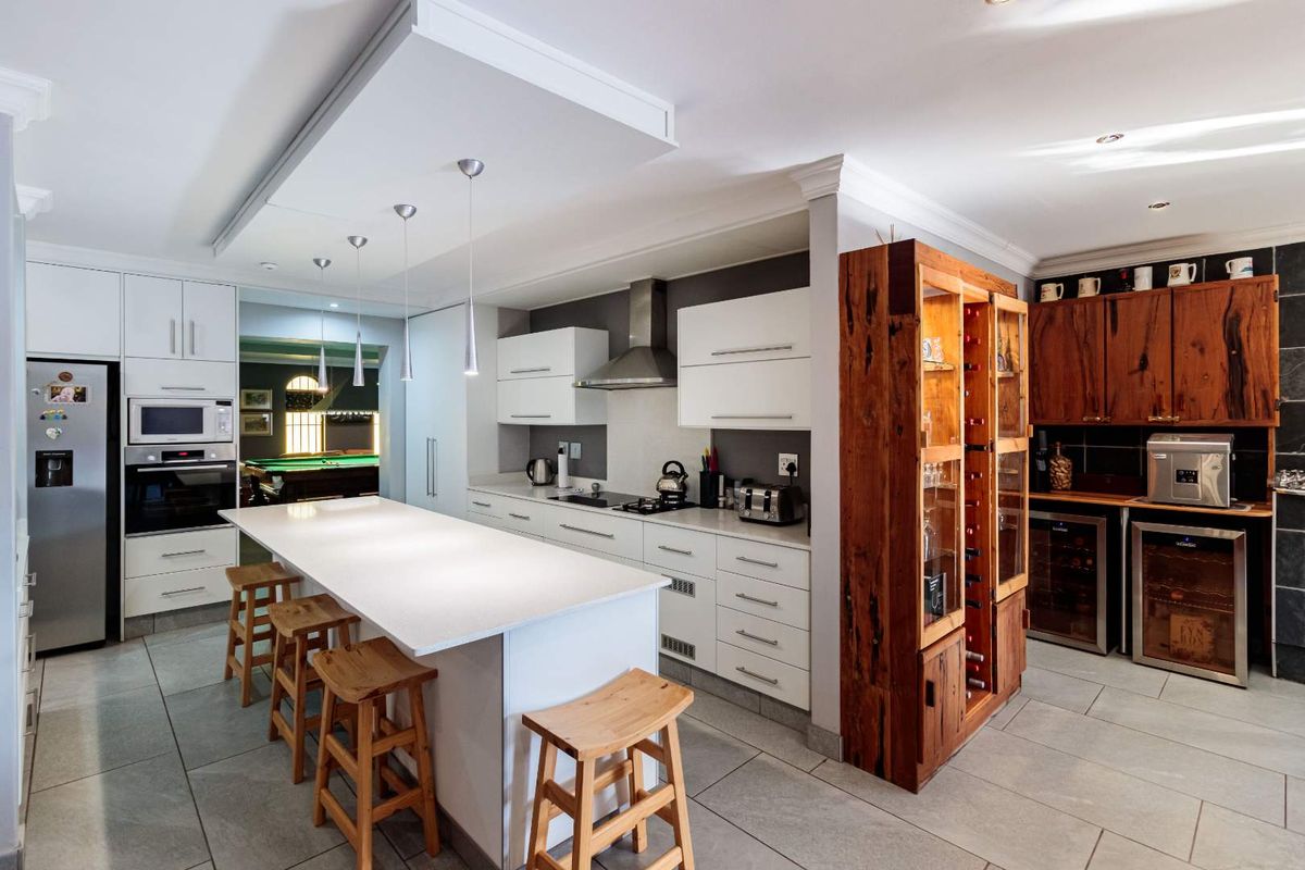 Modern kitchen featuring a central island, sleek white cabinetry, built-in appliances, and a dedicated wine storage area with tiled flooring throughout.