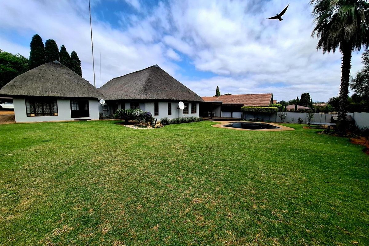Spacious rear garden featuring a well-maintained lawn, a swimming pool, and traditional thatch-roofed building structures.