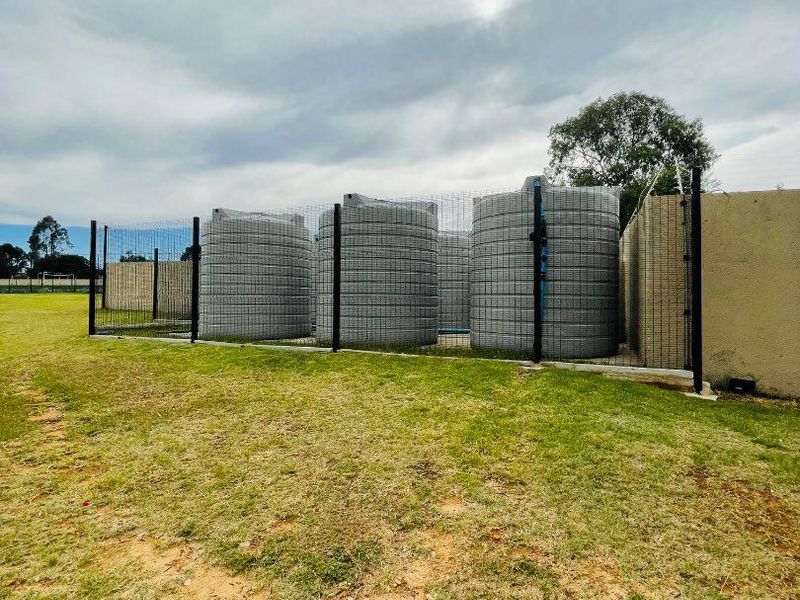 Outdoor utility area featuring multiple large water storage tanks enclosed within a secure wire mesh fence on a grassed plot.