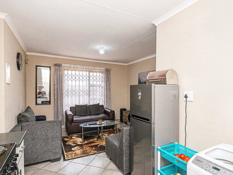 Open plan living area featuring tiled flooring and a security gate, seamlessly integrating the kitchen and lounge space.