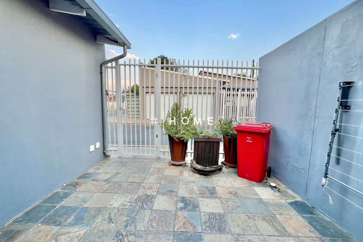 A paved outdoor courtyard area featuring a metal security gate, perimeter walls, and a wall-mounted clothes drying rack.