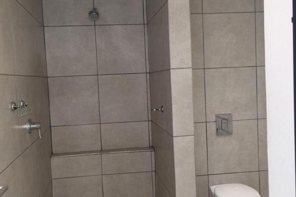 A modern bathroom featuring a walk-in shower with tiled flooring and a wall-mounted toilet with a concealed cistern.