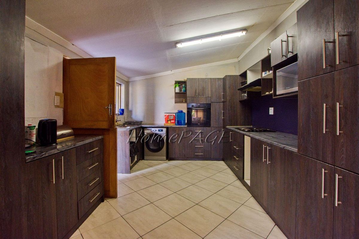 A functional kitchen featuring dark wood-look cabinetry, stone-effect countertops, tiled flooring, and integrated oven and hob.