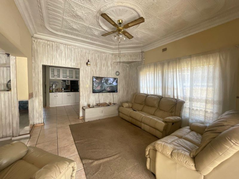 Open-plan living area featuring an ornate pressed metal ceiling, ceiling fan, and tiled flooring, with an adjacent kitchen visible through the doorway.