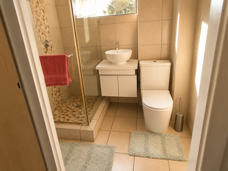 A compact, modern bathroom featuring a glass-enclosed shower with pebble tile flooring, a vessel sink on a floating vanity, and a standard toilet.
