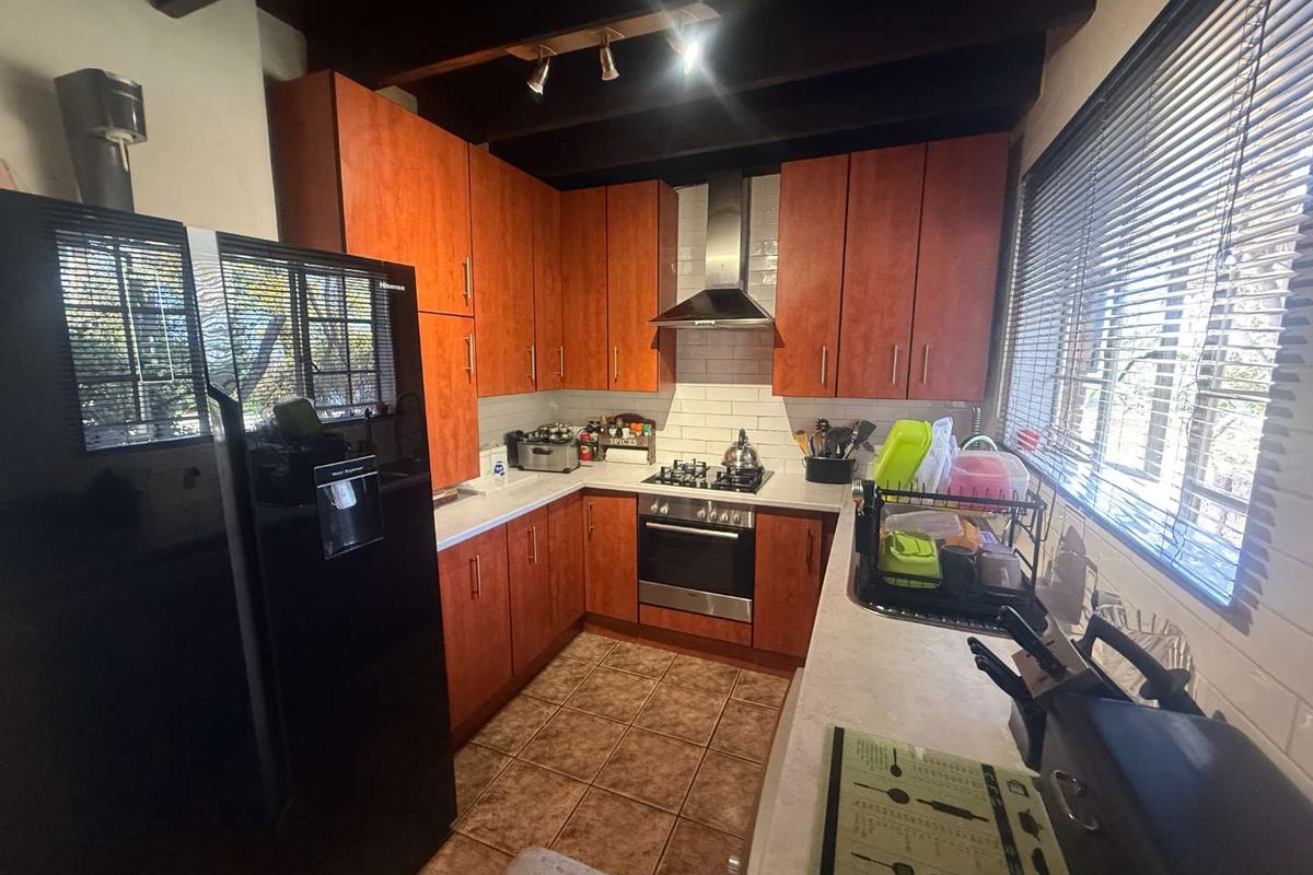 A functional kitchen featuring wood-finish cabinetry, a built-in oven, gas hob, stainless steel extractor fan, and tiled flooring with exposed ceiling beams.