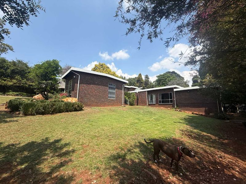 A view of the rear exterior of the face brick house, featuring a well-maintained lawn and established garden surroundings.