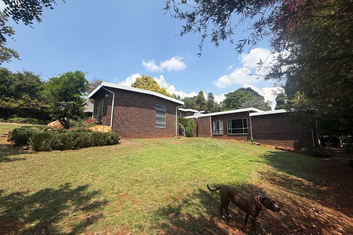 A view of the rear exterior of the face brick house, featuring a well-maintained lawn and established garden surroundings.