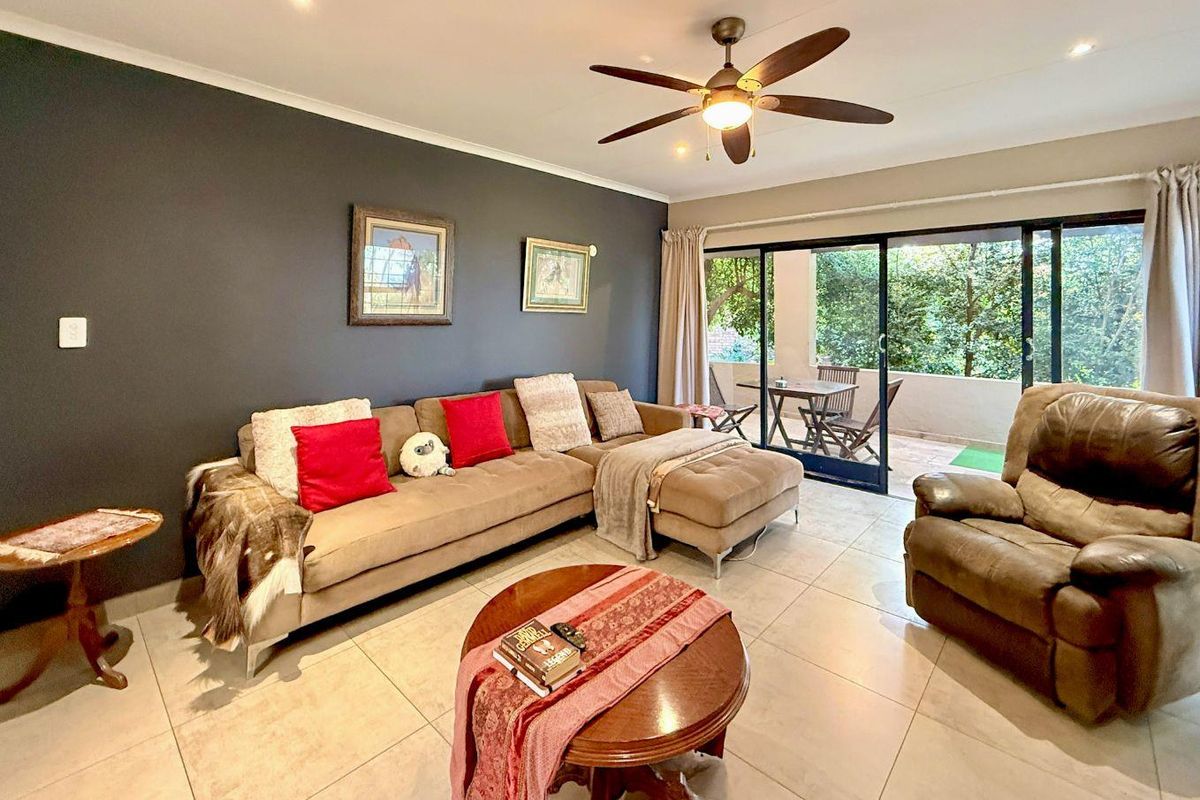 Spacious living room featuring large sliding glass doors that open onto a covered patio, tiled flooring, and a ceiling fan.
