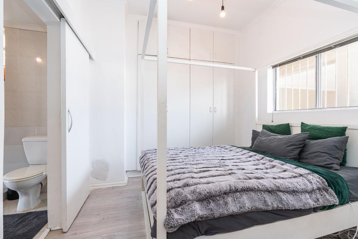 A bedroom featuring built-in cupboards and an en-suite bathroom with a toilet, finished with light-toned flooring.