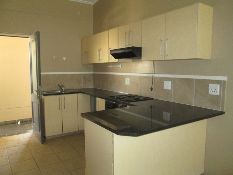 A functional kitchen featuring granite countertops, built-in cabinetry, an electric hob with extractor fan, and tiled backsplash, offering a clean and practical workspace.