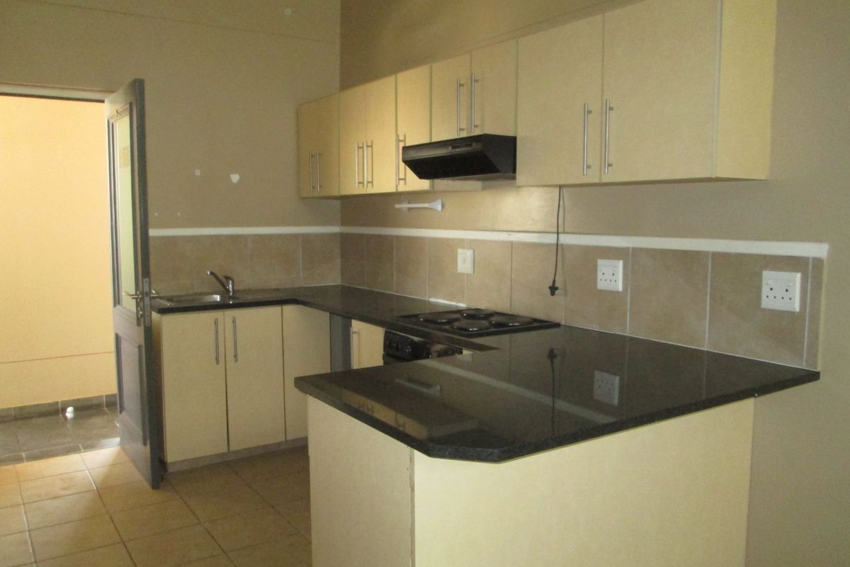 A functional kitchen featuring granite countertops, built-in cabinetry, an electric hob with extractor fan, and tiled backsplash, offering a clean and practical workspace.