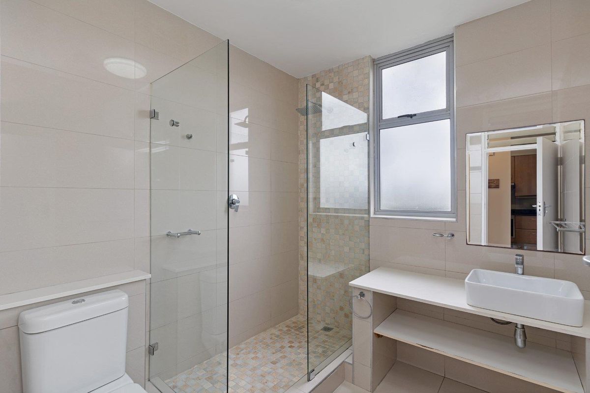Modern bathroom featuring a glass-enclosed shower with mosaic tiling, a wall-mounted basin, and neutral ceramic wall tiles.