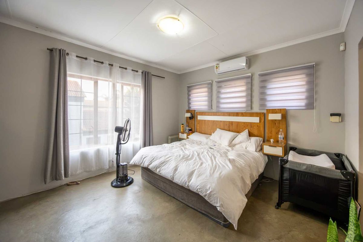 A well-lit bedroom featuring a built-in wooden headboard with integrated bedside tables, split-system air conditioning, and modern roller blinds.