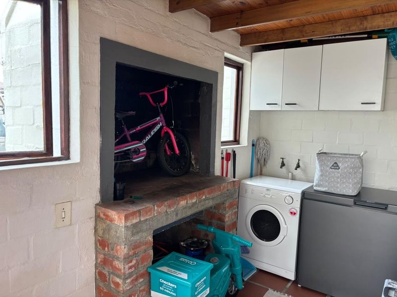 A functional laundry area featuring a built-in brick fireplace, exposed timber ceiling beams, and wall-mounted storage cabinetry.