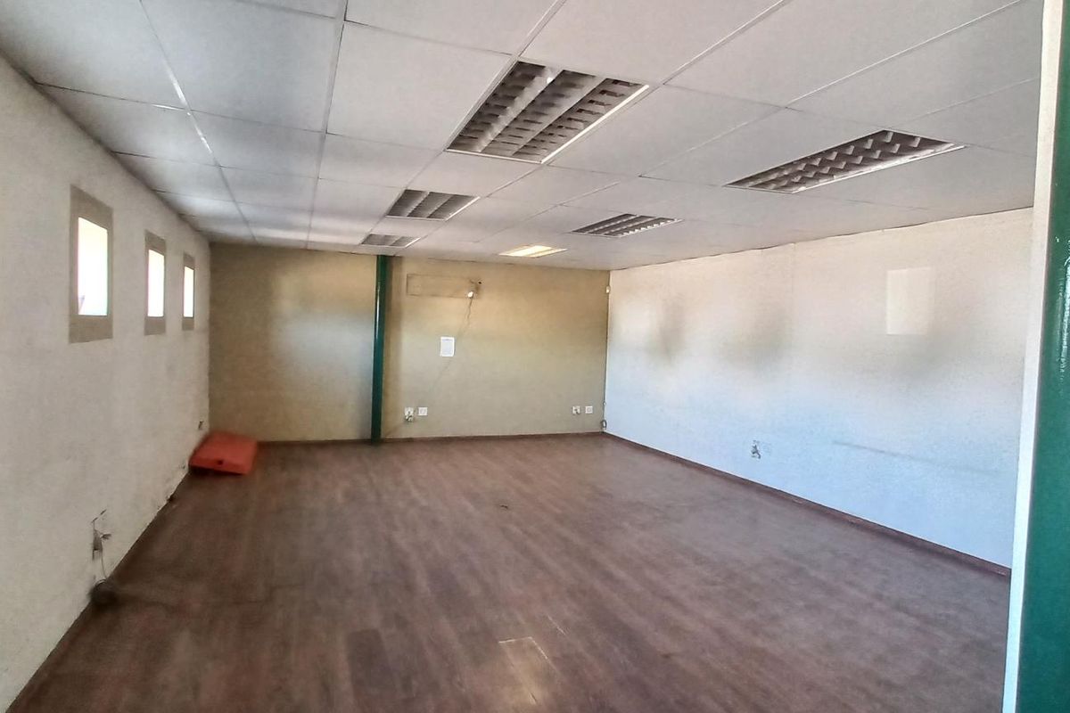 A spacious, open-plan industrial office or utility area featuring wood-look laminate flooring, recessed ceiling lighting, and multiple small square windows.