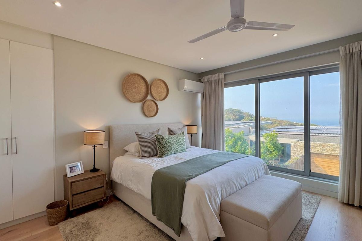 A well-maintained bedroom featuring built-in wardrobes, a ceiling fan, split-system air conditioning, and large sliding glass doors with views.