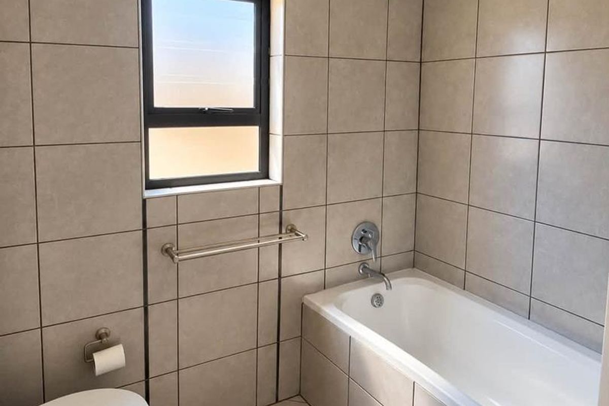 A clean, modern bathroom featuring neutral wall and floor tiles, a built-in bathtub with shower head, and standard sanitary fixtures.