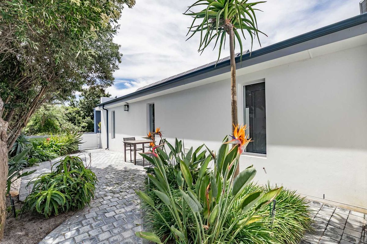 A well-maintained rear exterior featuring a paved patio area, established garden landscaping, and clean white wall finishes.