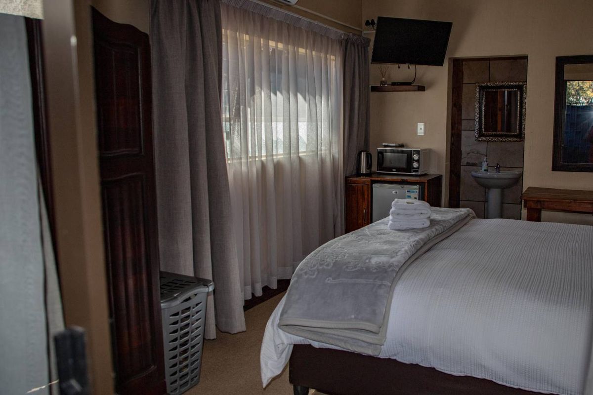A guest bedroom featuring an en-suite basin area, wall-mounted air conditioning unit, and carpeted flooring.