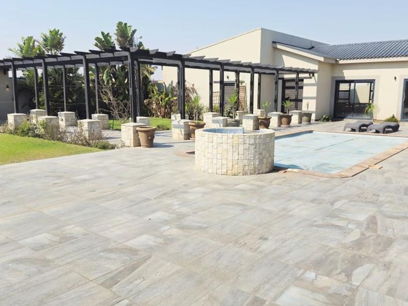 Spacious outdoor pool area featuring a stone-clad water feature, large paved patio, and a modern pergola structure, perfect for outdoor entertaining.