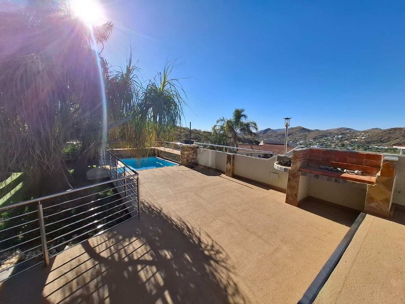Spacious outdoor patio area featuring a built-in braai, stainless steel balustrades, and a private swimming pool with scenic mountain views.