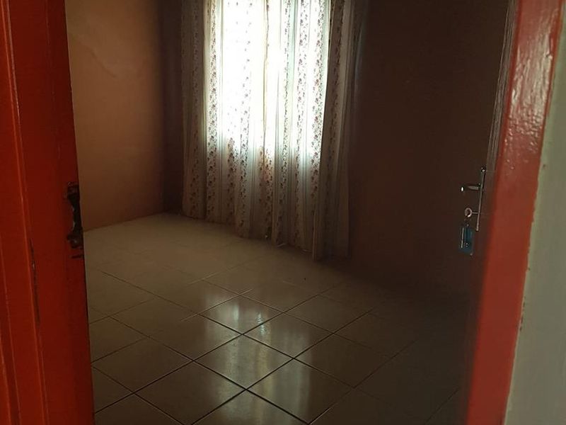 An empty bedroom featuring tiled flooring and a corrugated metal ceiling, offering a blank canvas for renovation and interior design updates.