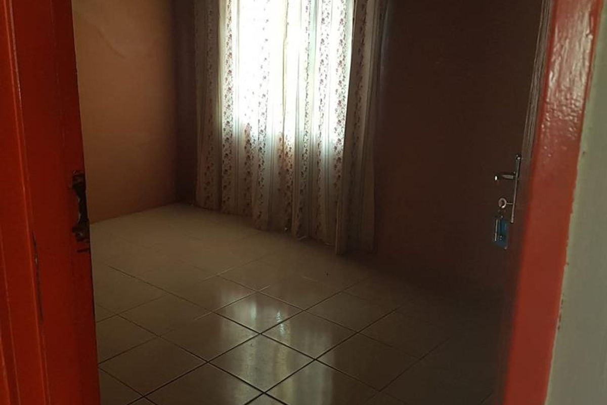 An empty bedroom featuring tiled flooring and a corrugated metal ceiling, offering a blank canvas for renovation and interior design updates.