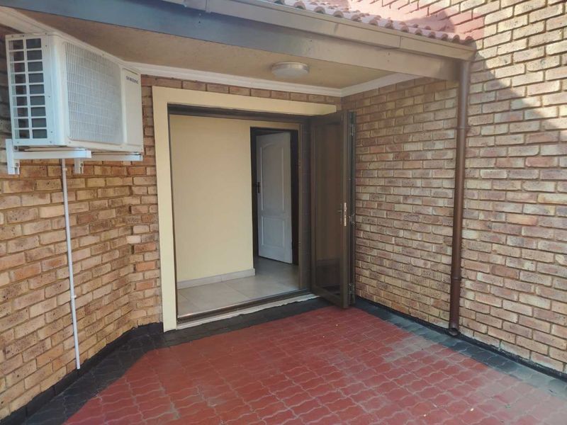 A covered outdoor patio area featuring exposed brick walls, paved flooring, and an external air conditioning unit, providing direct access to the interior.