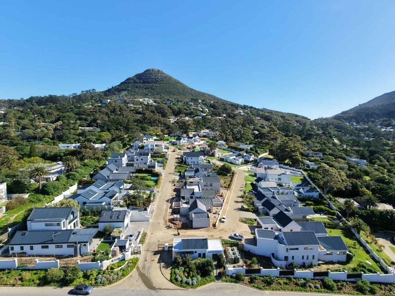 An aerial view of a modern residential estate featuring multiple homes with pitched roofs, paved streets, and surrounding mountain landscape.