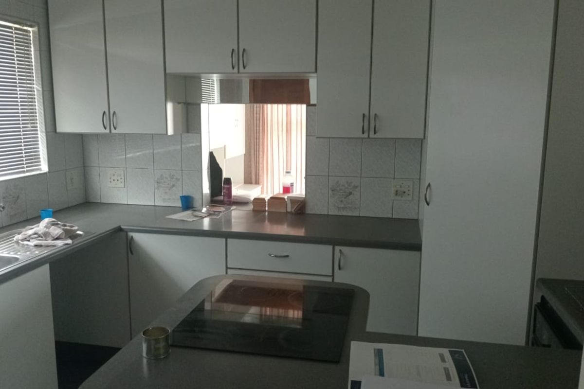 A functional kitchen featuring white cabinetry, tiled splashbacks, a built-in hob, and a stainless steel sink with a window view.