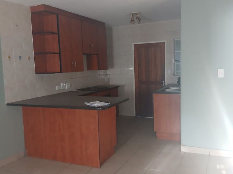 A functional kitchen featuring wooden cabinetry, laminate countertops, a double sink, and tiled flooring, offering a clean and practical layout.