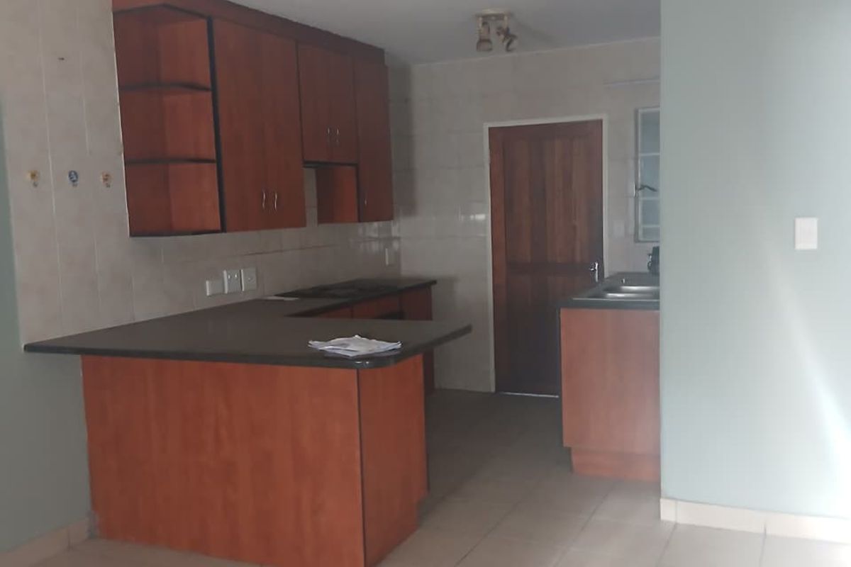 A functional kitchen featuring wooden cabinetry, laminate countertops, a double sink, and tiled flooring, offering a clean and practical layout.