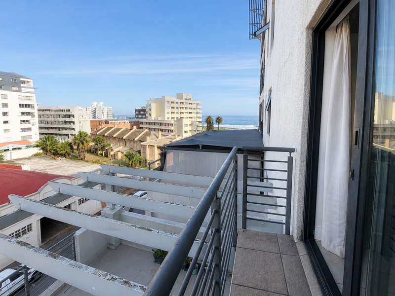 A balcony featuring tiled flooring, a metal railing, and a pergola structure, offering an elevated view of the surrounding urban area and coastline.