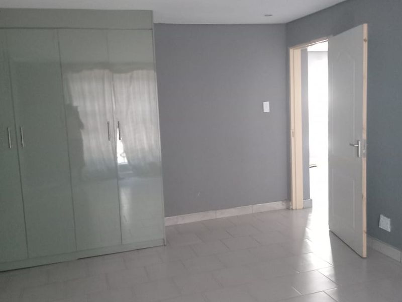 A vacant bedroom featuring neutral grey walls, tiled flooring, and built-in cupboards, offering a clean and versatile space.