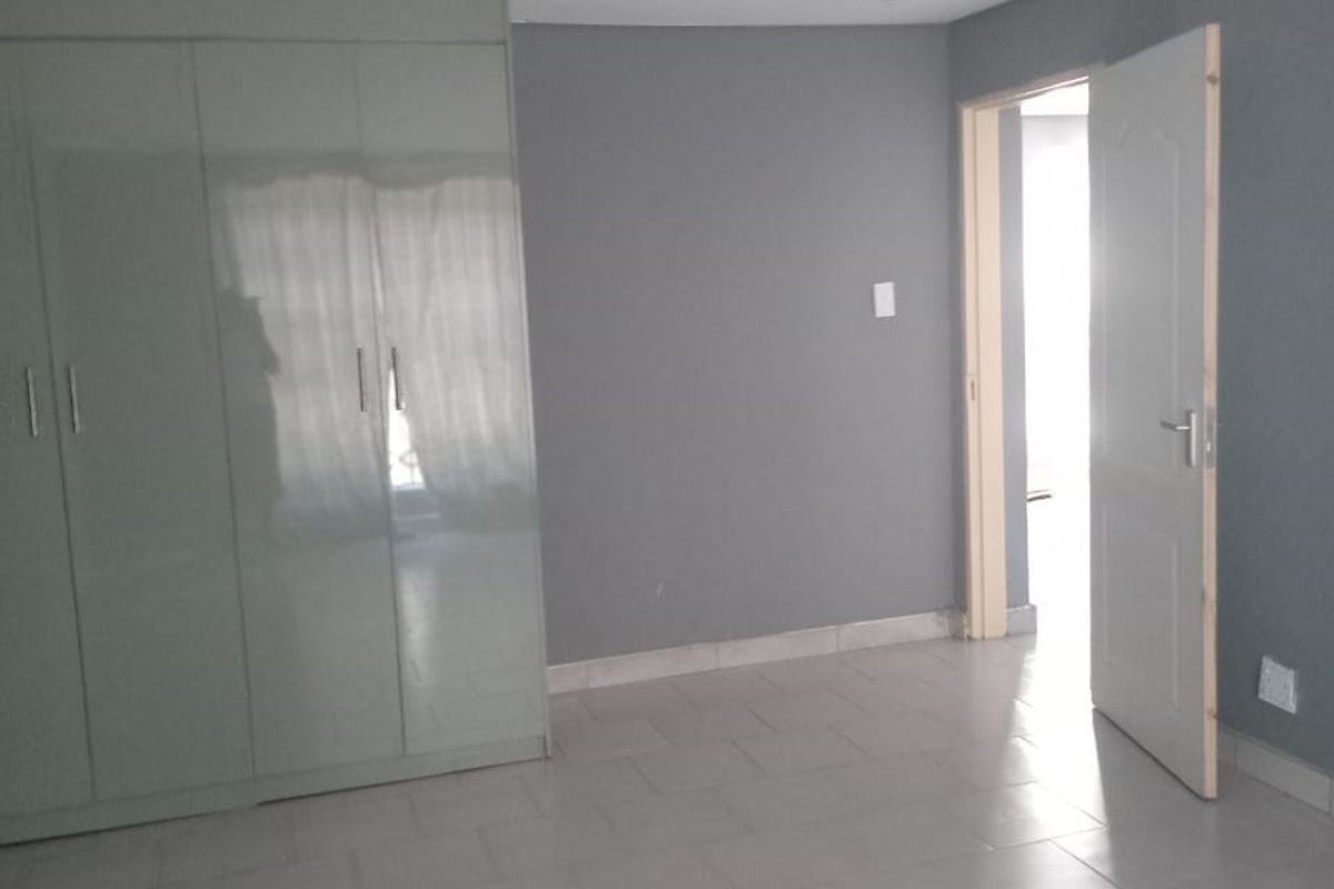 A vacant bedroom featuring neutral grey walls, tiled flooring, and built-in cupboards, offering a clean and versatile space.