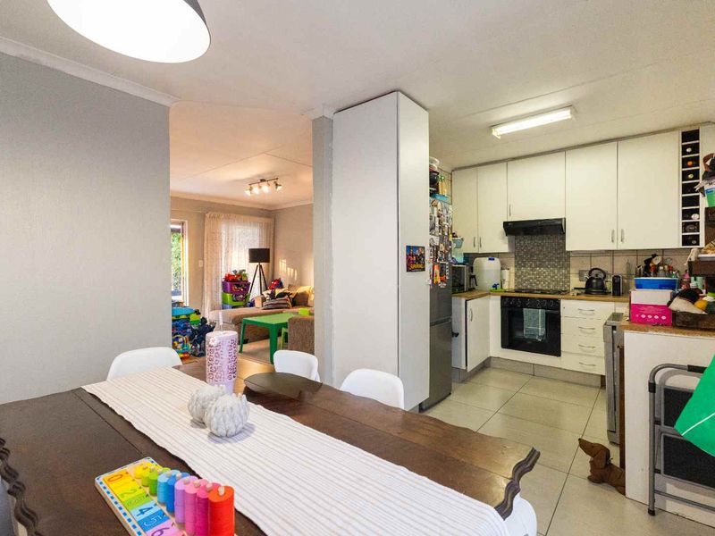 Open-plan kitchen and dining area featuring white cabinetry, built-in oven, hob, extractor fan, and tiled flooring, flowing into the adjacent living space.