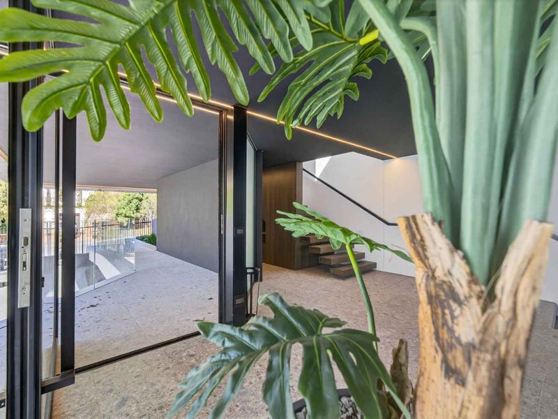 Modern entrance hall featuring a floating staircase, glass balustrade, recessed LED lighting, and seamless indoor-outdoor flow through large sliding glass doors.
