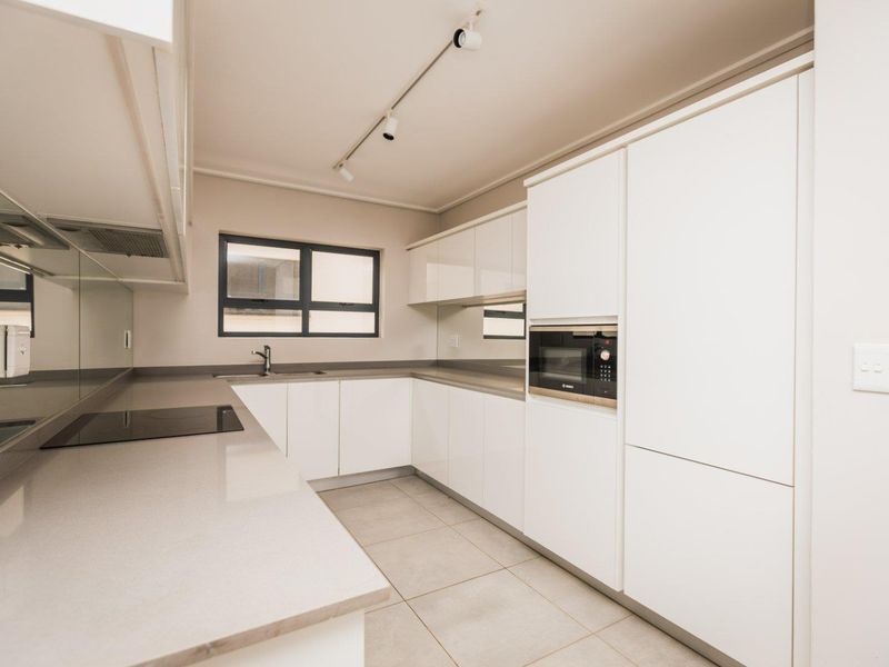 Modern, minimalist kitchen featuring sleek white cabinetry, stone countertops, integrated appliances, and neutral tiled flooring in a clean, well-lit space.